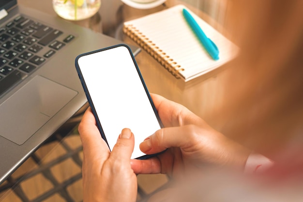 Closeup photo female using smartphone with blank white screen mobile phone mockup concept in warm tones background