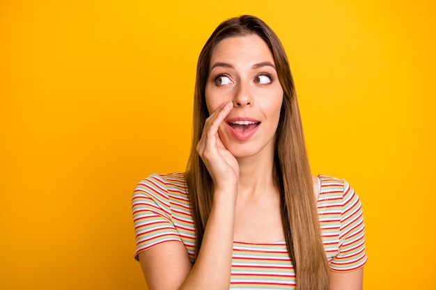 Closeup photo of funny lady holding hand near mouth looking empty space cunning sharing fresh news chatterbox person wear casual striped t-shirt isolated yellow color wall