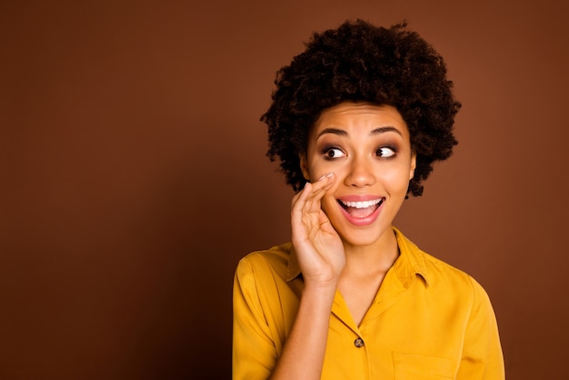 Closeup photo of funny pretty dark skin wavy lady holding hand near mouth sharing gossips rumours with crowd people wear yellow shirt isolated brown color