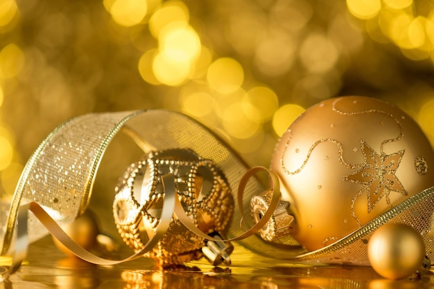 Closeup photo of gold christmas tree decorations ornaments balls serpentine and ribbon on golden bokeh background