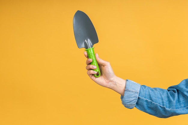 Closeup photo of green shovel in woman's hand isolated over yellow background