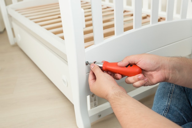 Closeup photo of handyman tightening the screws on white wooden bed