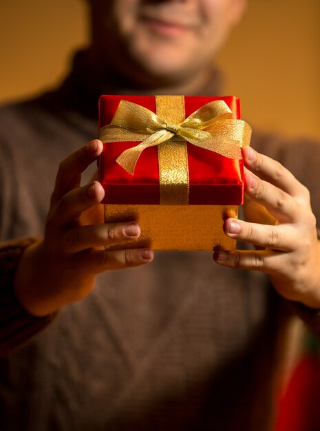 Closeup photo of happy man holding red gift box with golden bow