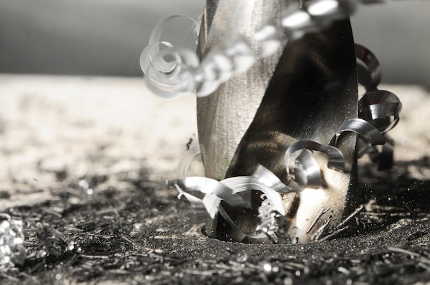 Closeup photo of hole drilling process, metal shavings around drill.