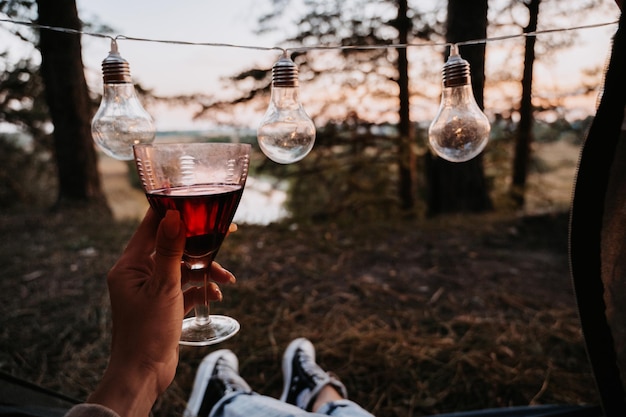 A closeup photo of the intentions of women's legs The girl has a glass of wine or water in her hands The concept of a tourist trekking expedition View from the tent to the landscape