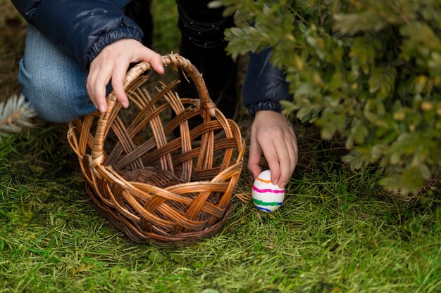 Крупным планом фото маленькой девочки кладет красочные пасхальные яйца в корзину