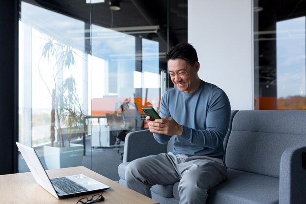 Closeup photo of male businessman using phone in modern office asian looking at phone display and smiling online call