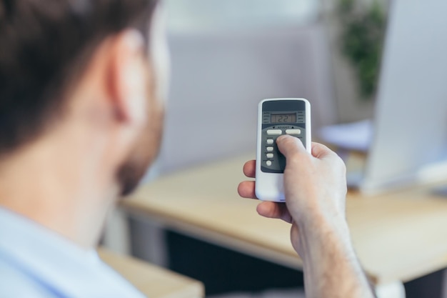 Closeup photo of a man's hand holding an air conditioner remote control changing the temperature businessman working in a bright office