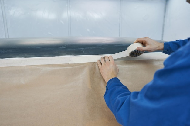 Closeup photo of mechanic holding white tape and sealing car body preparing it before painting in service center