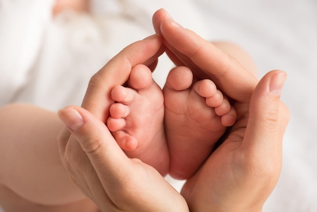 Closeup photo of newborn's feet in mother's palms on isolated white textile background