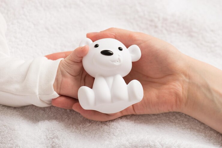 Photo closeup photo of newborn's tiny hand in mother's hand holding white smiling bear toy on isolated white textile background