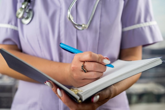 Foto foto del primo piano di un'infermiera in uniforme che tiene un diario e prende appunti in un ospedale