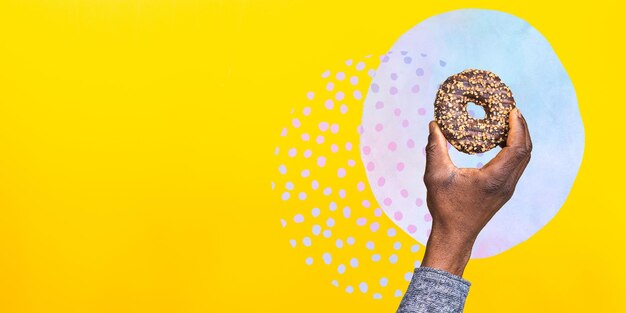 Фото Крупным планом фото руки афроамериканца, держащего пончик нездоровая пища векторная иллюстрация коллажа