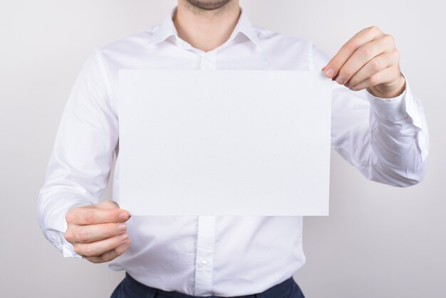 Closeup photo portrait of handsome serious guy holding white clear clean paper board in hands isolated grey background copyspace