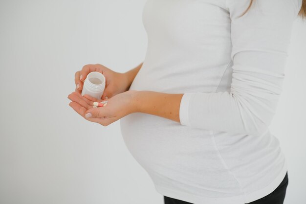 Closeup photo of pregnant woman holding pills and medicine bottle