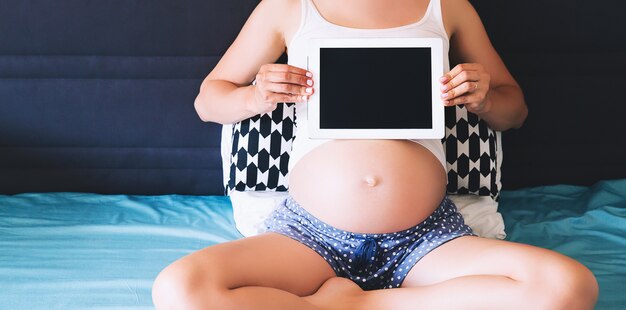 Closeup photo of pregnant woman holding and showing blank tablet screen at home