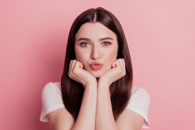 Foto del primo piano di una ragazza carina che invia baci d'aria mani drean toccano il mento isolato sfondo di colore rosa brillante