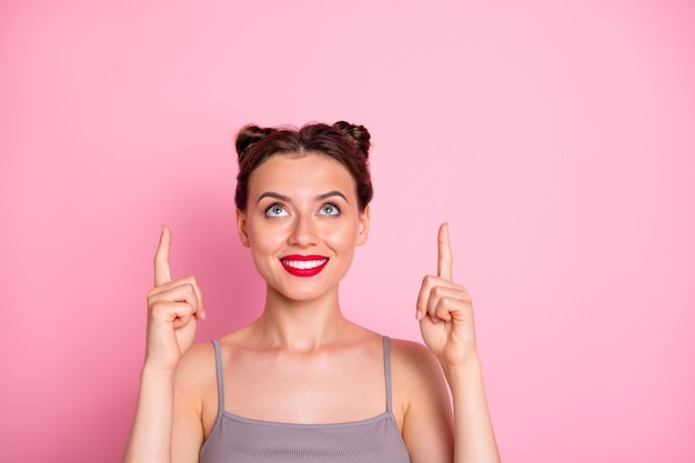 Closeup photo of pretty millennial lady funny buns red pomade indicating fingers up empty space best shopping prices wear casual grey tank-top isolated pink color