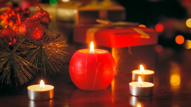 Крупным планом фото красной свечи, горящей на деревянном столе, украшенном на Рождество