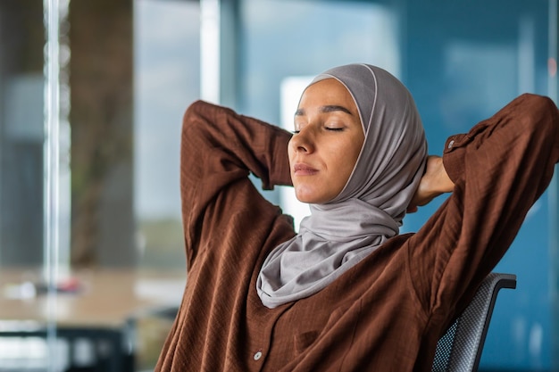 Closeup photo relaxed young businesswoman in hijab sitting in the office she threw her hands behind