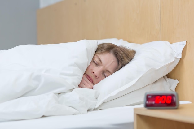 Фотография крупным планом бессонной и расстроенной женщины, лежащей в постели под одеялом и пытающейся заснуть