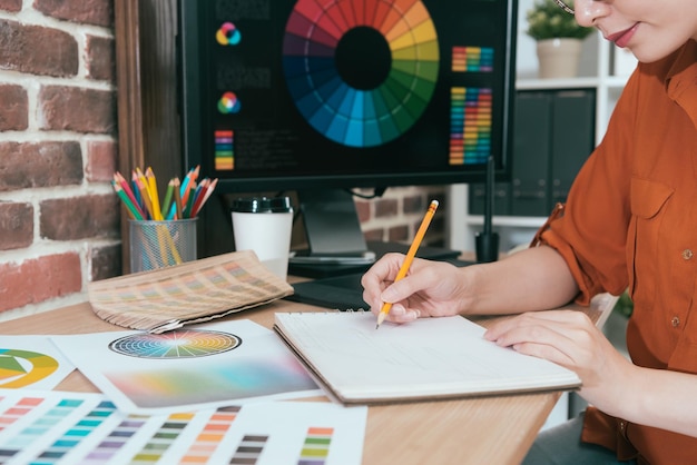 closeup photo of smiling pretty girl designer using pencil drawing sketch on empty notebook and creating new design works.