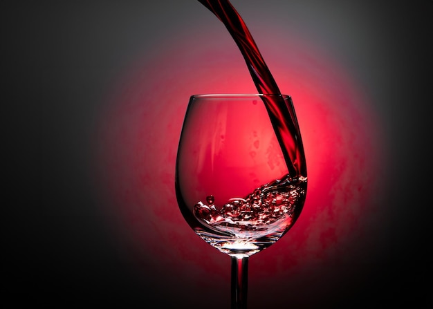 Foto foto in close-up di vino versato in un bicchiere di vino su sfondo nero con illuminazione rossa