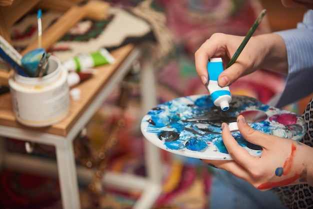 Closeup photo of a woman painting on canvas with a brush and tempera