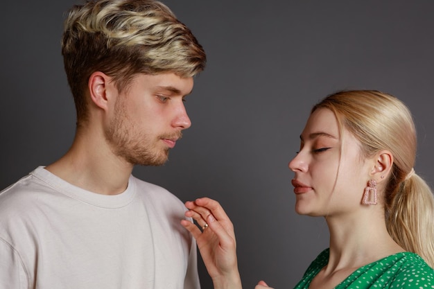 Closeup photo of young couple standing on Gray background and young man looking at his girlfriend while she closed her eyes