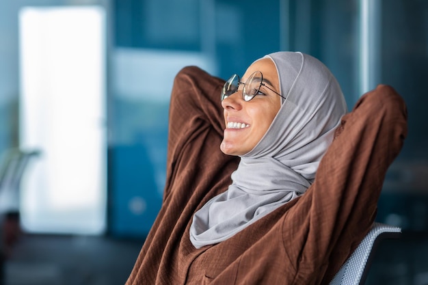 Closeup photo young female student in hijab and glasses she sits leaning on a chair contentedly