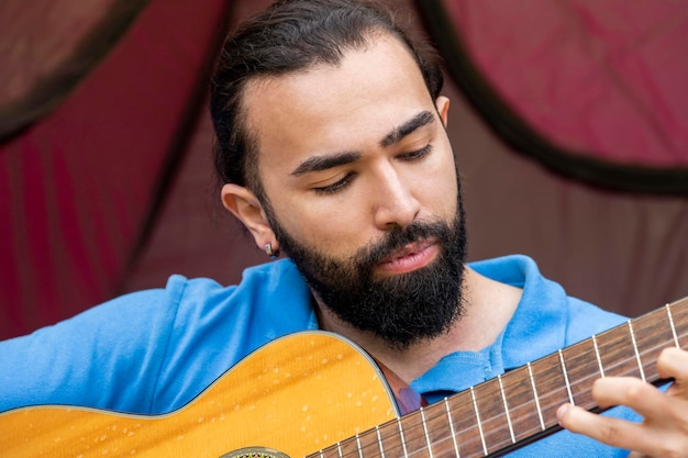 Closeup photo of young man playing guitar at the camping