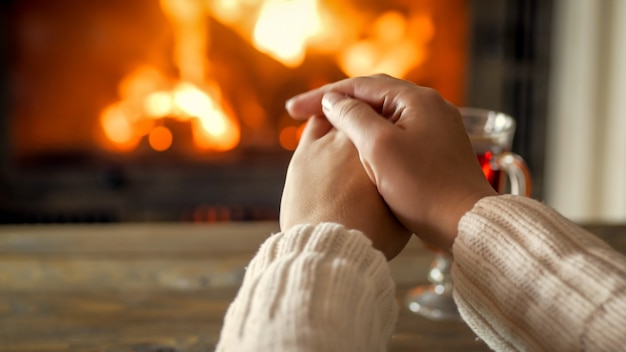 Closeup photo of young woman warming hands by the burning fireplace at house