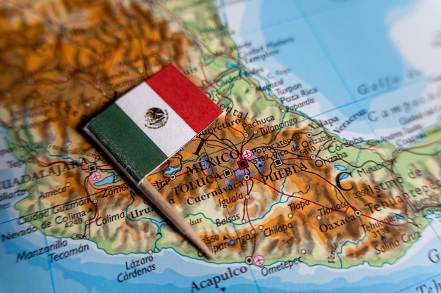 Closeup photograph of Mexicos national flag positioned on a topographical map showing Mexico City Toluca Puebla and other central Mexican cities with surrounding terrain