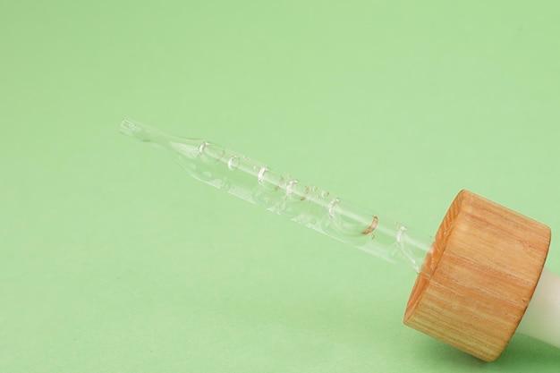 Closeup photography of the pipette with dripping oil.Zero waste wooden cover,pastel background.Cosmetics mockup concept.