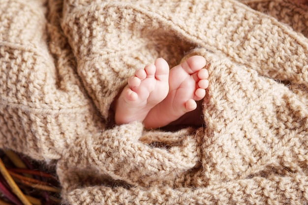 Closeup picture of newborn baby feet on beige knitted plaid. Fine concept of the childhood and motherhood