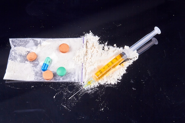 様々 な薬と黒の背景の薬物使用と中毒の概念に注射器の山をクローズ アップ