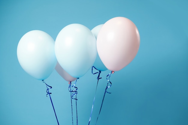 Closeup of pink and blue helium balloons on blue surface with soft shadows and copy space