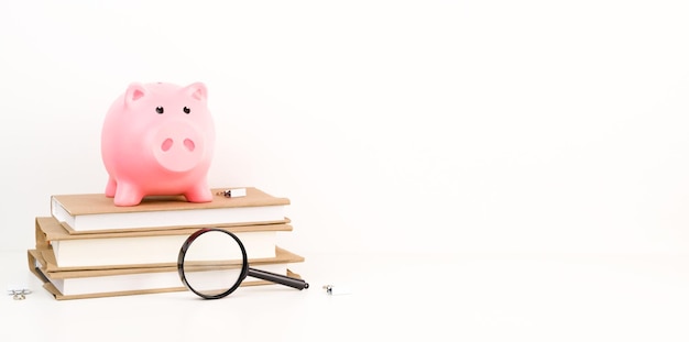 Closeup of Pink Piggy bank on top of books with magnifier as concept of the cost of education or research Education or research fundScholarship conceptBanner with place for text