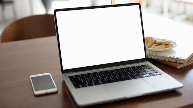 Closeup A portable laptop computer white screen mockup on wooden office desk