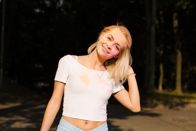 Closeup portrait of adorable blonde woman in white t shirt with color paint covered her face at Holi Festival