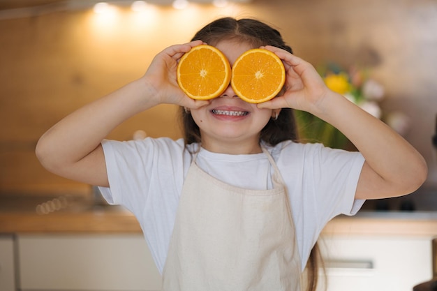 Closeup portrait of adorable little girl in apron stand in kitchen and smiling child holding halves