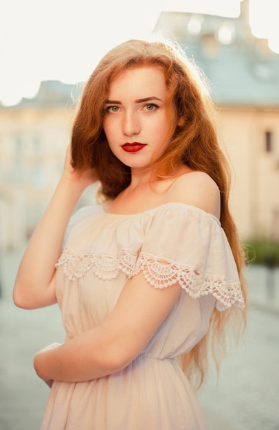 Closeup portrait of adorable red haired woman with naked shoulders posing at the city street