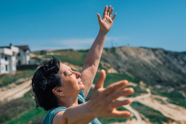 Closeup portrait of an adult woman on a mountain with a smile on her face raising her hands to the