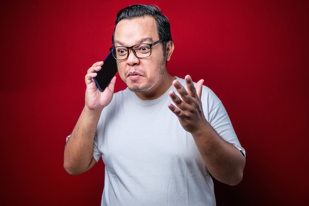 Photo closeup portrait angry young asian man, guy mad student, pissed off employee shouting while on phone isolated red background. negative human emotion face expression feeling attitude