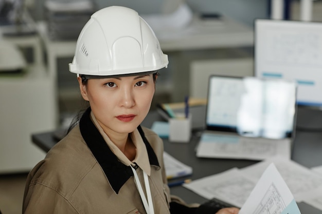 Closeup portrait of Asian woman wearing hardhat at workplace in office and looking at camera copy space