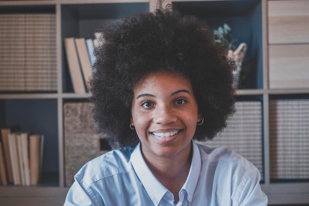 Closeup portrait of attractive dark skinned young woman with curly Afro hairstyle African american businesswoman smiling at office Young positive lady smiling and looking at camera