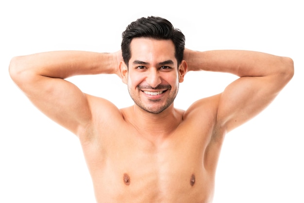 Closeup portrait of a attractive male model with muscular body standing with hands behind his head and smiling on white background