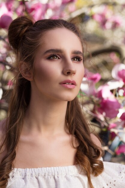 Closeup portrait of awesome brunette woman standing in blooming magnolia garden