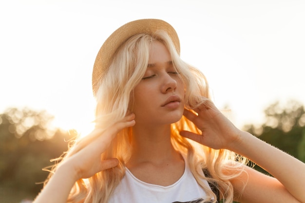 Ritratto del primo piano di una bella donna bionda con capelli biondi ricci e cappello di paglia