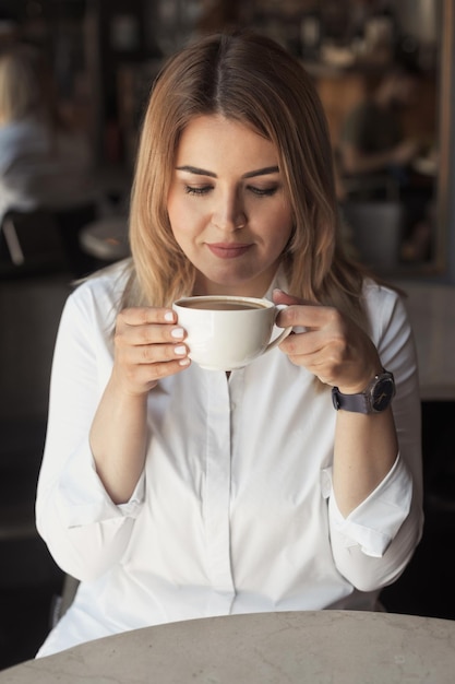 Photo closeup portrait of a beautiful business woman in white office shirt drinking morning coffee